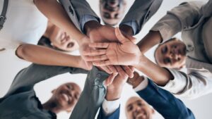 Groupe de collègues en cercle joignant leurs mains au centre dans un geste de cohésion.