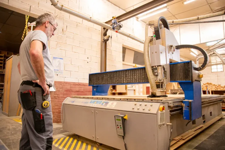 Ouvrier observant une machine CNC en fonctionnement dans un atelier de menuiserie industriel.