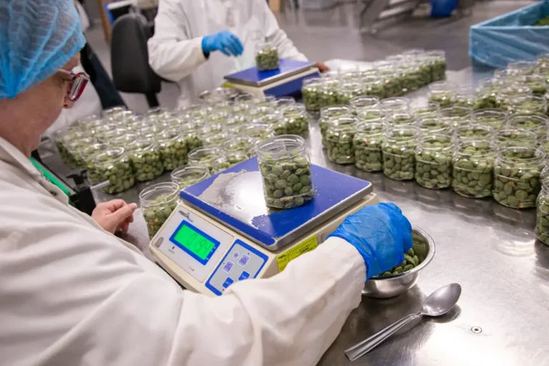 Technicienne en blouse blanche pesant un bocal d'olives vertes sur balance numérique, usine.